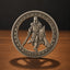 A circular silver-toned coin or medallion featuring a knight in armor holding a sword and shield, standing on a wooden surface against a dark background. The coin is inscribed with 'E.