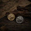 Gold and silver bald eagle signet rings placed side by side on a wood surface with both engraved faces visible, photographed in warm natural light showing the color contrast between the two finishes