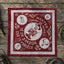 Burgundy red bandana laid flat on a wooden surface showing the same white Bandido skull cowboy line-art with Wanted Dead or Alive text and four corner medallions