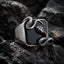 Close-up of a black onyx signet ring on dark rock showing a silver serpent coiled around the square stone with the snake head raised at the upper corner and detailed scale texture visible