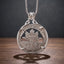 caduceus wolf coin pendant necklace — winged caduceus with double serpents, wolf and maple leaf landscape, Cultivating Altruism banner inscription, four-prong open frame, ornate skull bail, antique silver tone, dark wood surface