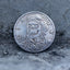 Close-up of a coin engraved with a skull in aviator goggles and flight jacket, Liberty and In God We Trust inscriptions, dated 1942, on dark stone