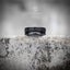 Angled view of black oxidized Soviet coin ring showing partial Cyrillic anniversary text — worn-in dark finish, historical relic aesthetic on weathered stone