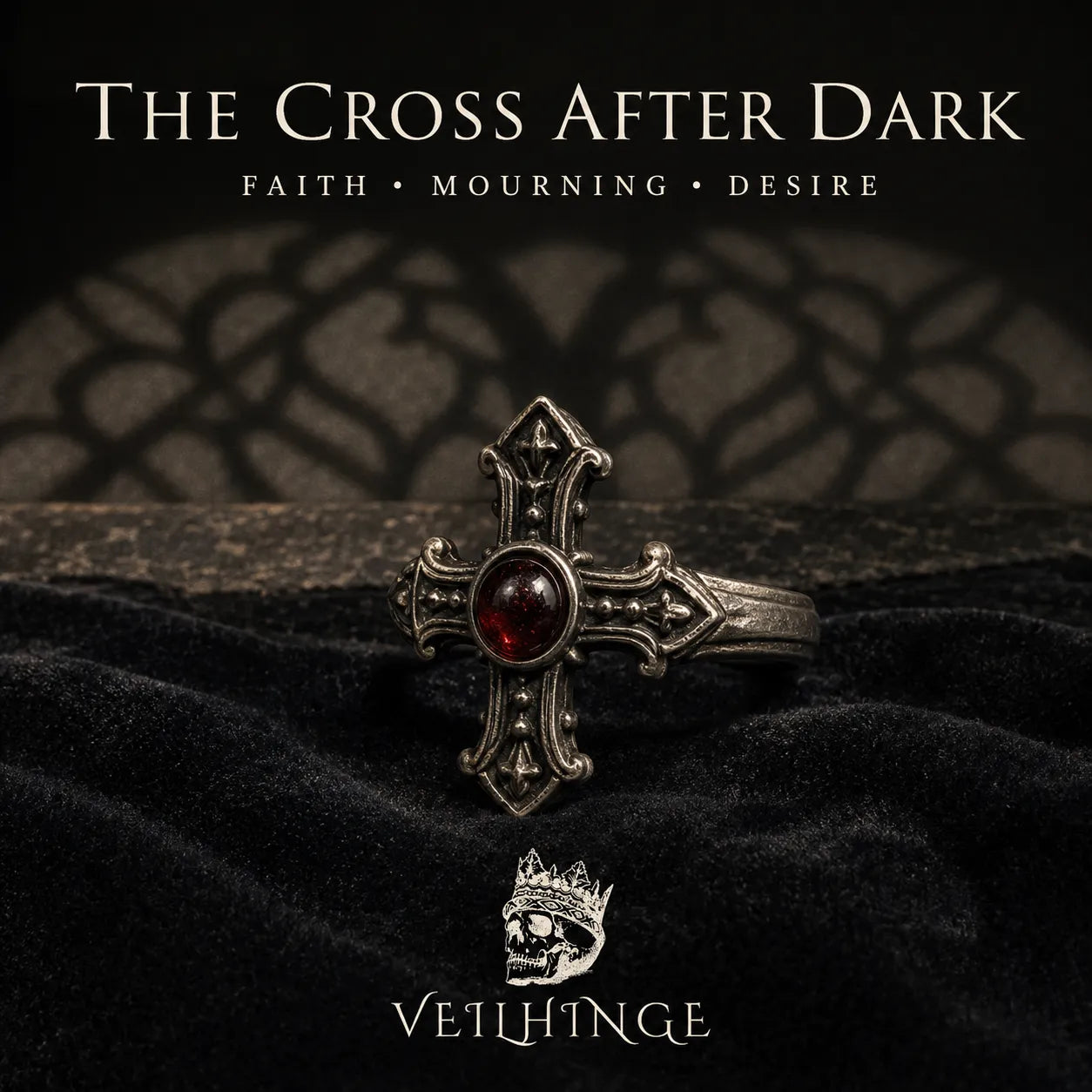 Blackened silver cross ring with a deep red garnet resting on black velvet beneath the title The Cross After Dark.