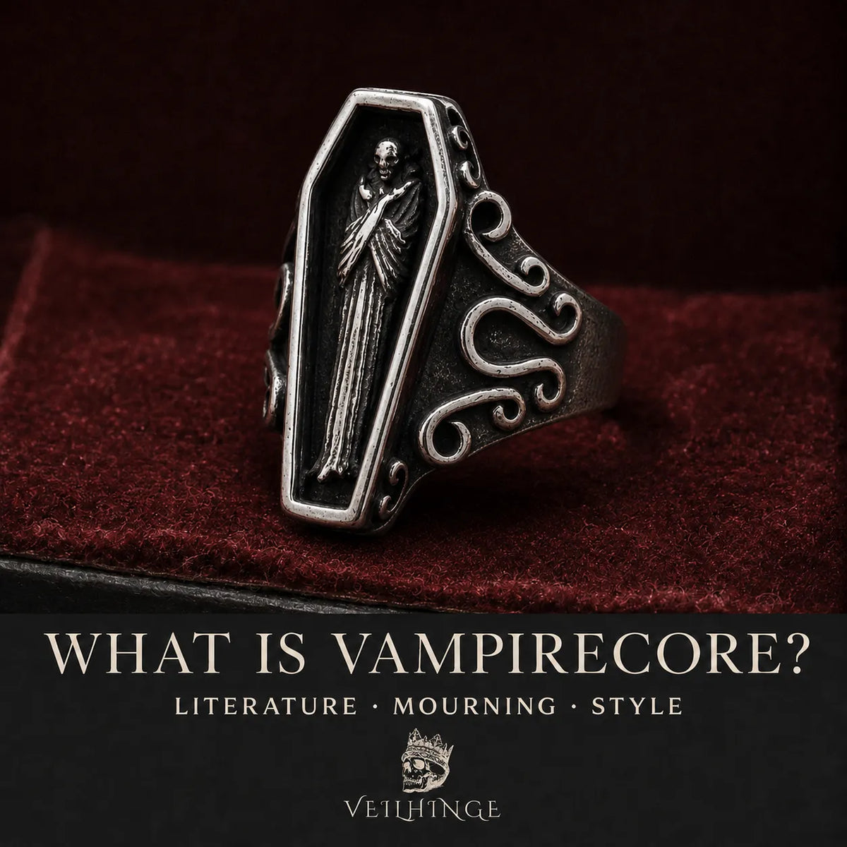 Oxidized silver coffin ring featuring a hooded skeletal figure and Baroque scrollwork on dark red velvet.