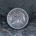 A round silver-toned coin or medallion featuring a detailed central figure and the text 'E PLURIBUS UNUM' around the edge, with '1899' at the bottom, photographed on a dark textured surface.