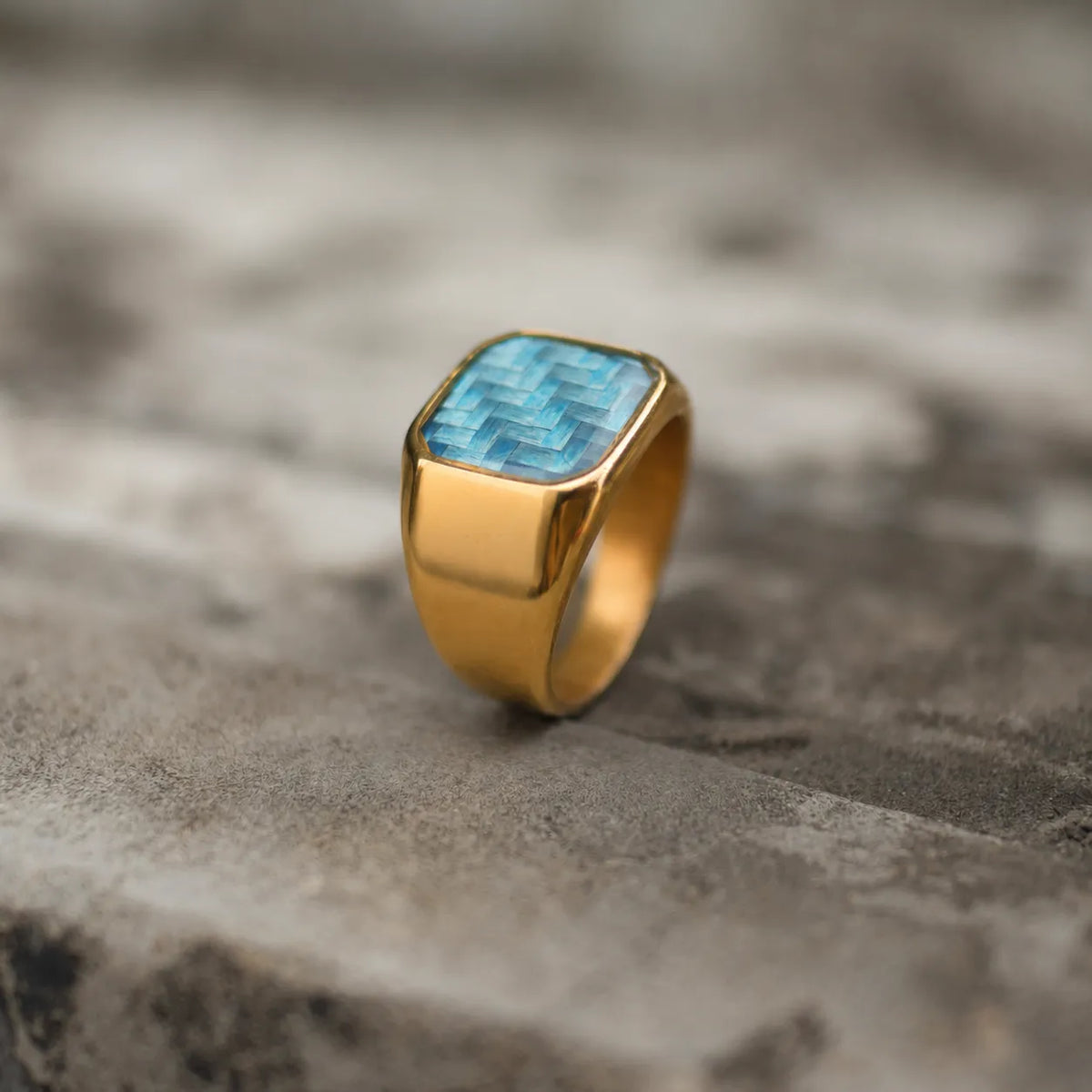 Three-quarter view of an 18K gold-plated signet ring with a blue woven face