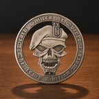 A circular silver-toned metal challenge coin featuring a skull wearing a beret, with the engraved text 'Death Smiles At Everdone' and 'Army Smiles Back' around the border, standing on a wooden surface against a dark background.