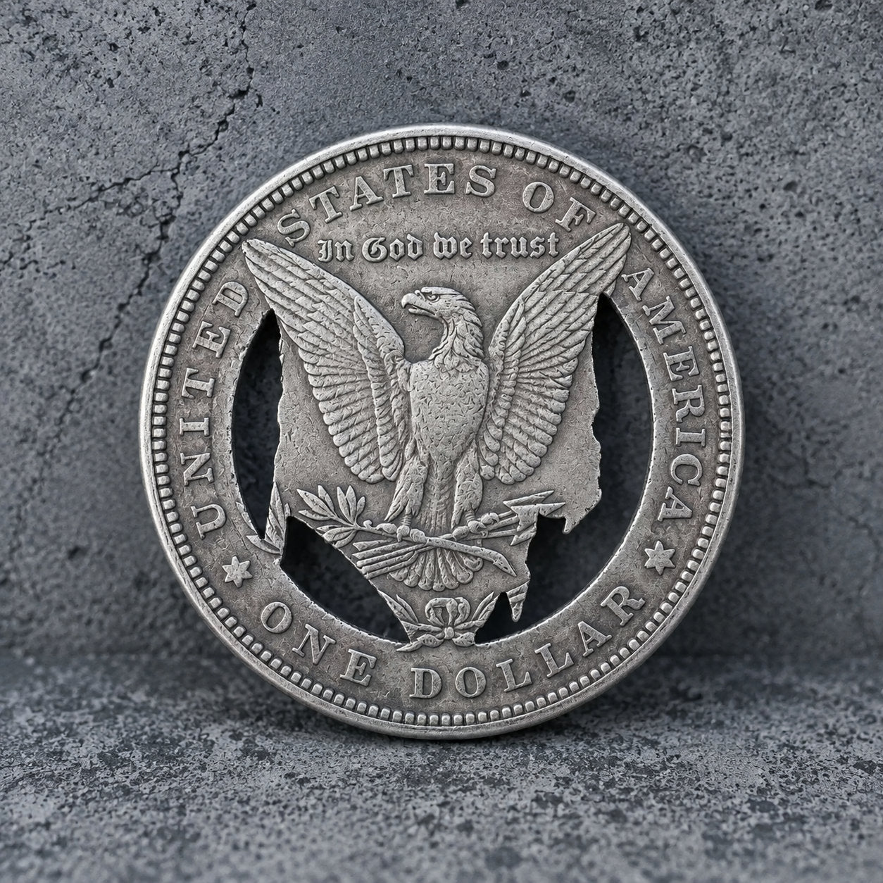 A silver-colored United States one dollar coin featuring an eagle design, photographed against a textured gray concrete background.