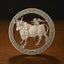 A circular silver-toned metal plaque featuring a detailed relief of a bull with a figure riding it, displayed on a dark wooden surface against a dark background.