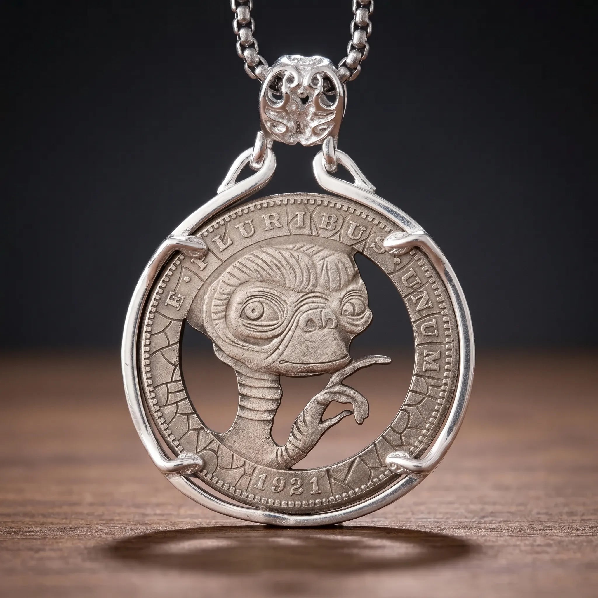 E.T. hobo coin pendant necklace — alien portrait hand-cut on 1921 coin face, E pluribus unum inscription, four-prong open frame, skull bail, antique silver tone, dark wood surface