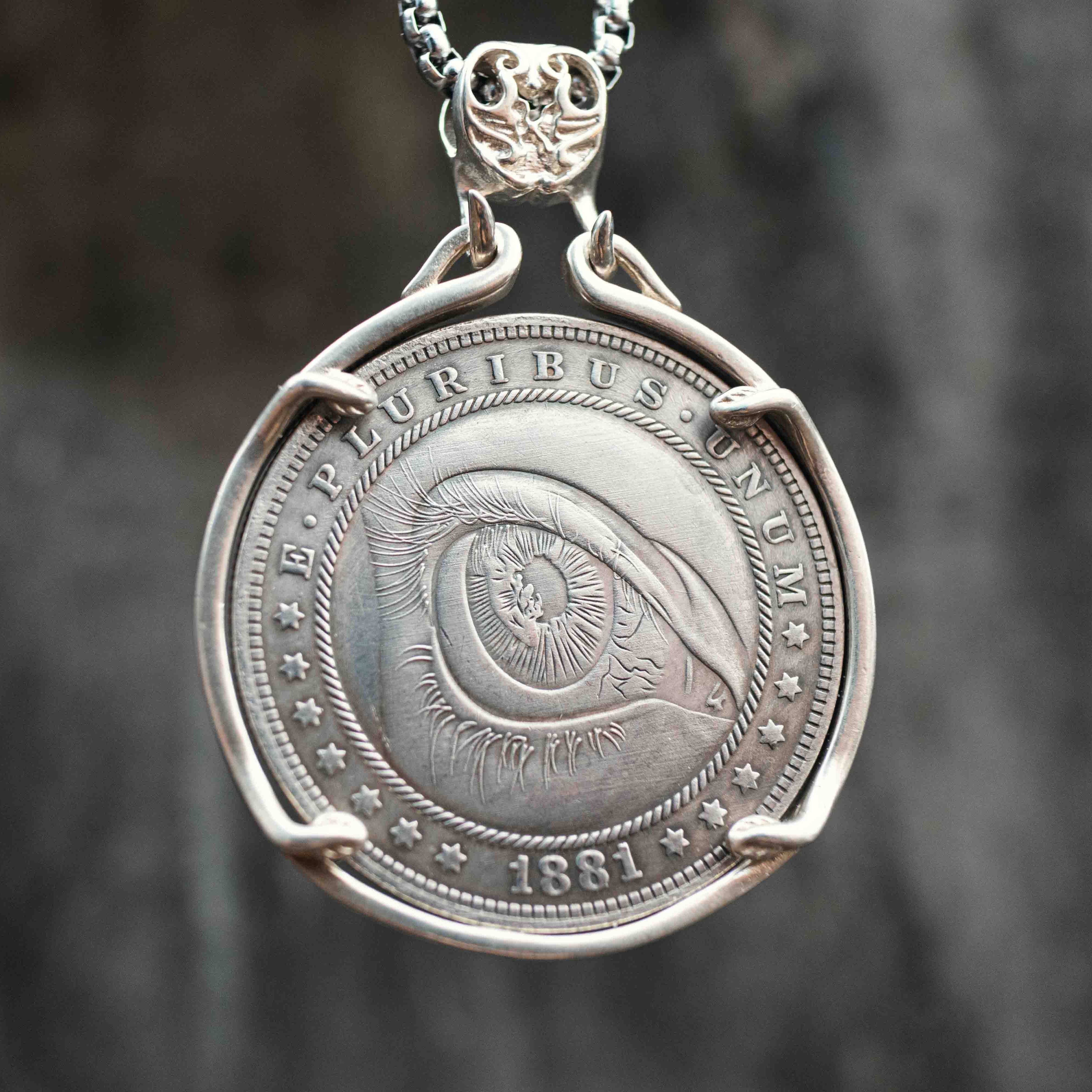 Coin pendant engraved with a large all-seeing eye with iris detail and concentric ripple rings filling the entire face, dated 1881, set in a four-prong bezel on a chain Main image