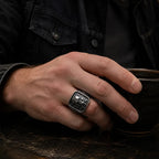Man wearing an antique silver rectangular skull signet ring in a dark vintage café setting