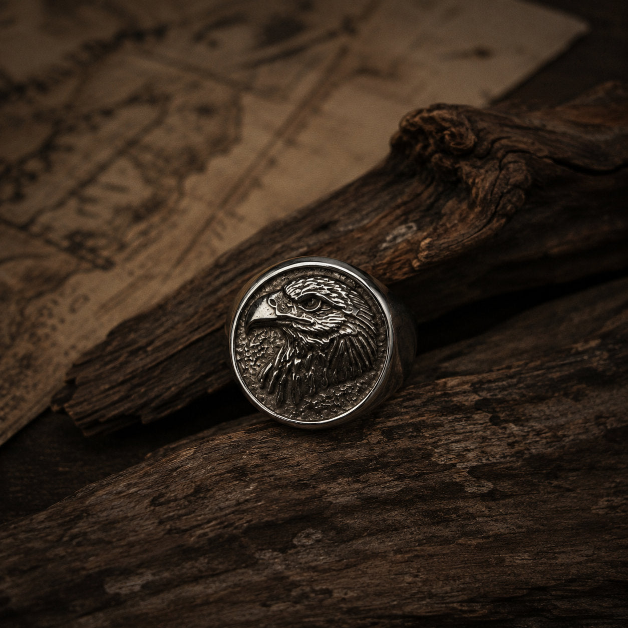 Antique silver eagle head signet ring resting on a dark wood surface, showing the raised bald eagle engraving detail with oxidized shadow in the feather and eye recesses