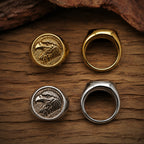 Four eagle signet rings arranged on a wood surface showing both gold and silver colorways from the front engraved face and the plain back band side by side