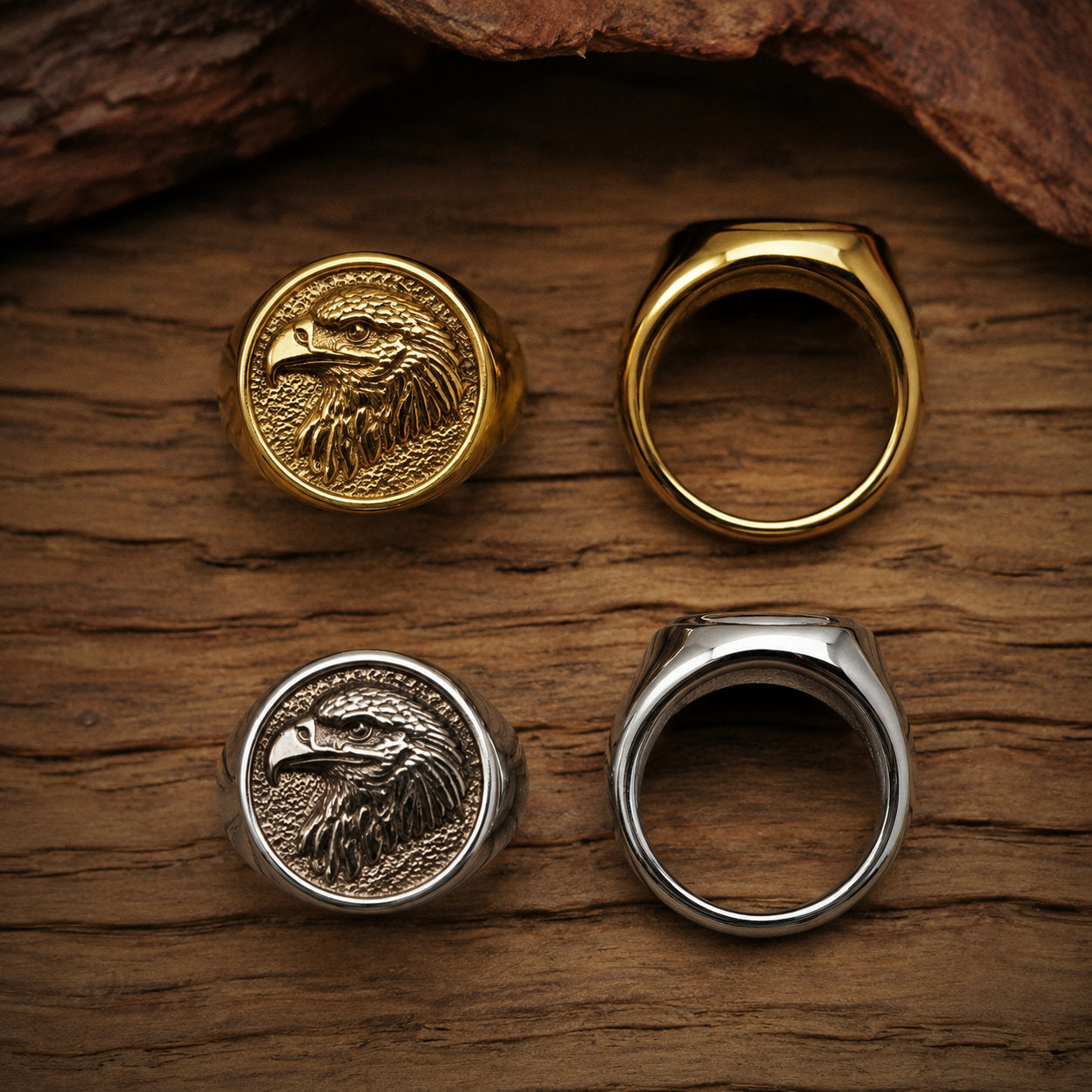 Four eagle signet rings arranged on a wood surface showing both gold and silver colorways from the front engraved face and the plain back band side by side