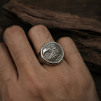 Man's hand wearing an antique silver bald eagle signet ring on the index finger, photographed against a dark wood surface in side lighting