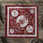 Burgundy red bandana laid flat on a wooden surface showing the same white Bandido skull cowboy line-art with Wanted Dead or Alive text and four corner medallions