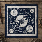 Navy blue bandana laid flat on a wooden surface showing white line-art of a skeleton cowboy on horseback surrounded by circular medallions with a raven, skull, and bull head, with the text Wanted Dead or Alive and Se Usa Un Bandido Tu Pañuelo