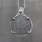 Coin pendant engraved with a baroque skull with flowing curly hair and scrollwork details, spine below, Liberty inscription, dated 1964, in a four-prong bezel on a chain