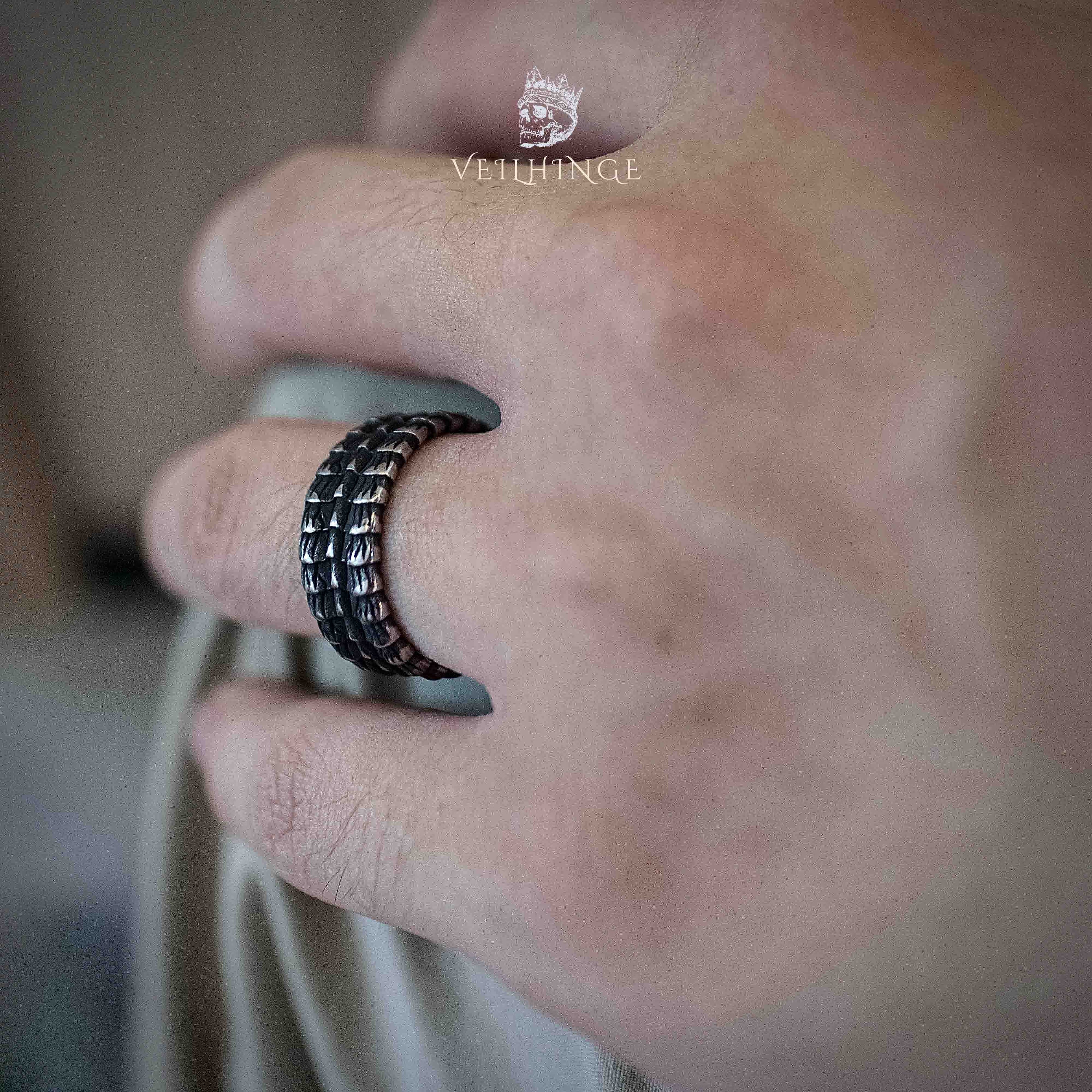 Wide black band ring with layered dragon scale texture worn on a middle finger, matte black finish with raised scale pattern visible from a side angle