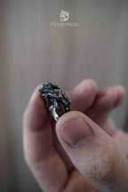 Black thorn branch ring held between fingers showing the full ring structure, interlocking dark metal thorns wrapping the entire band