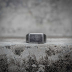 Blank signet ring with sandblasted matte rectangular face in oxidized black stainless steel, minimalist dark aesthetic ring by Veilhinge, front view
