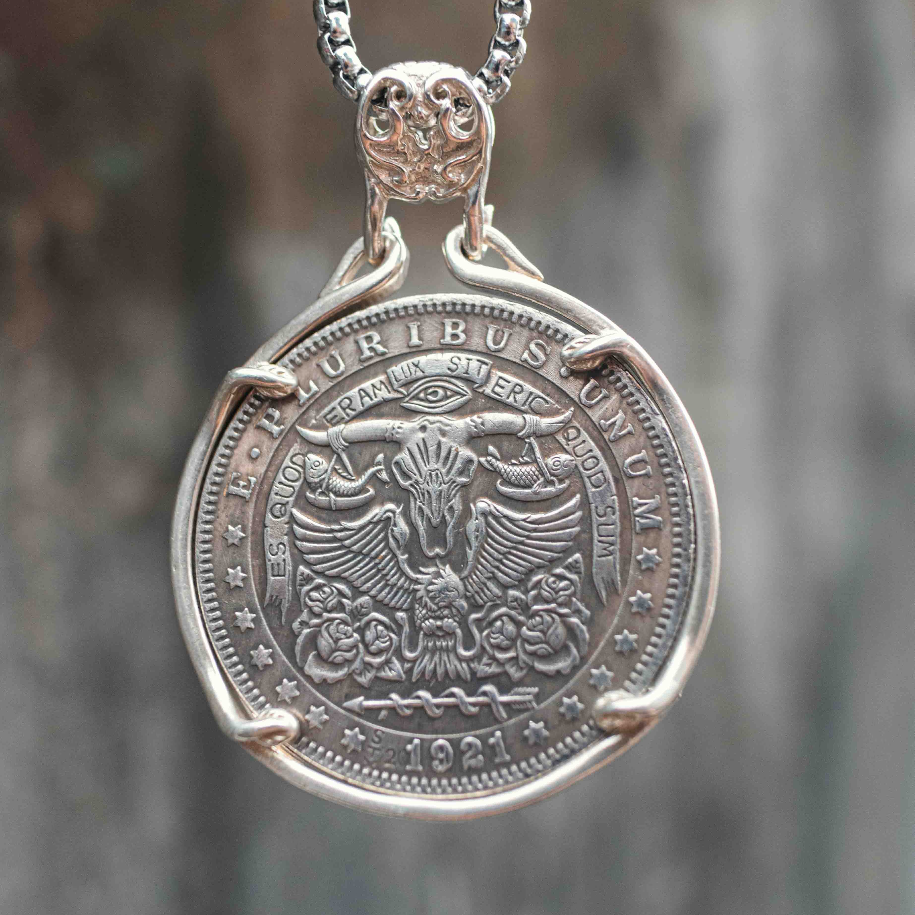 Coin pendant engraved with a bull skull below the Eye of Providence, flanked by spread wings and rose details, dated 1921, set in a four-prong bezel on a box chain