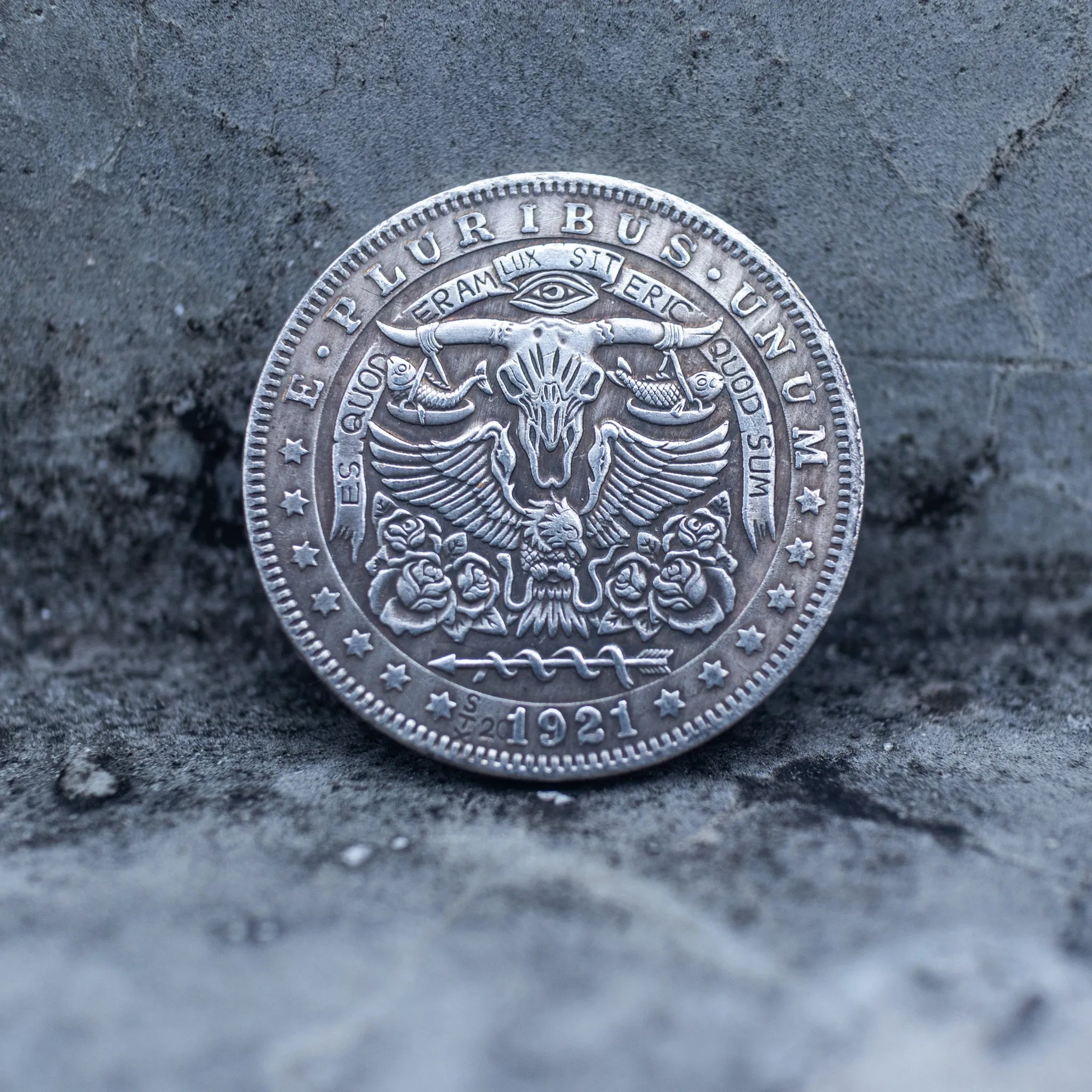 Close-up of a coin engraved with a horned bull skull, Eye of Providence above, spread wings on either side, rose motifs below, E Pluribus Unum border, dated 1921