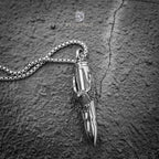 bullet pendant with eagle talon grip laid on cracked stone surface — side angle showing chain and sculptural detail