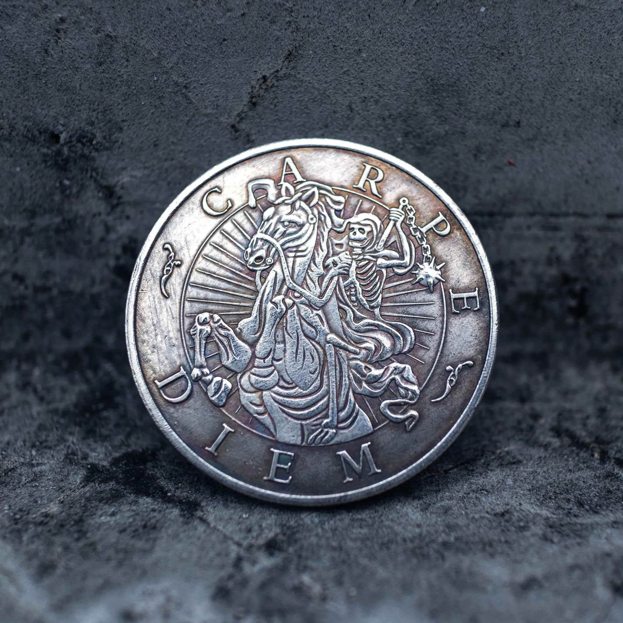 Hand-engraved Carpe Diem coin with skeletal reaper figure, photographed on dark slate surface