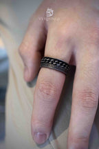 Chain spinner ring viewed from below showing Roman numeral inscription along the lower band edge, dark oxidized metal with bronze tones and rotating chain layer above