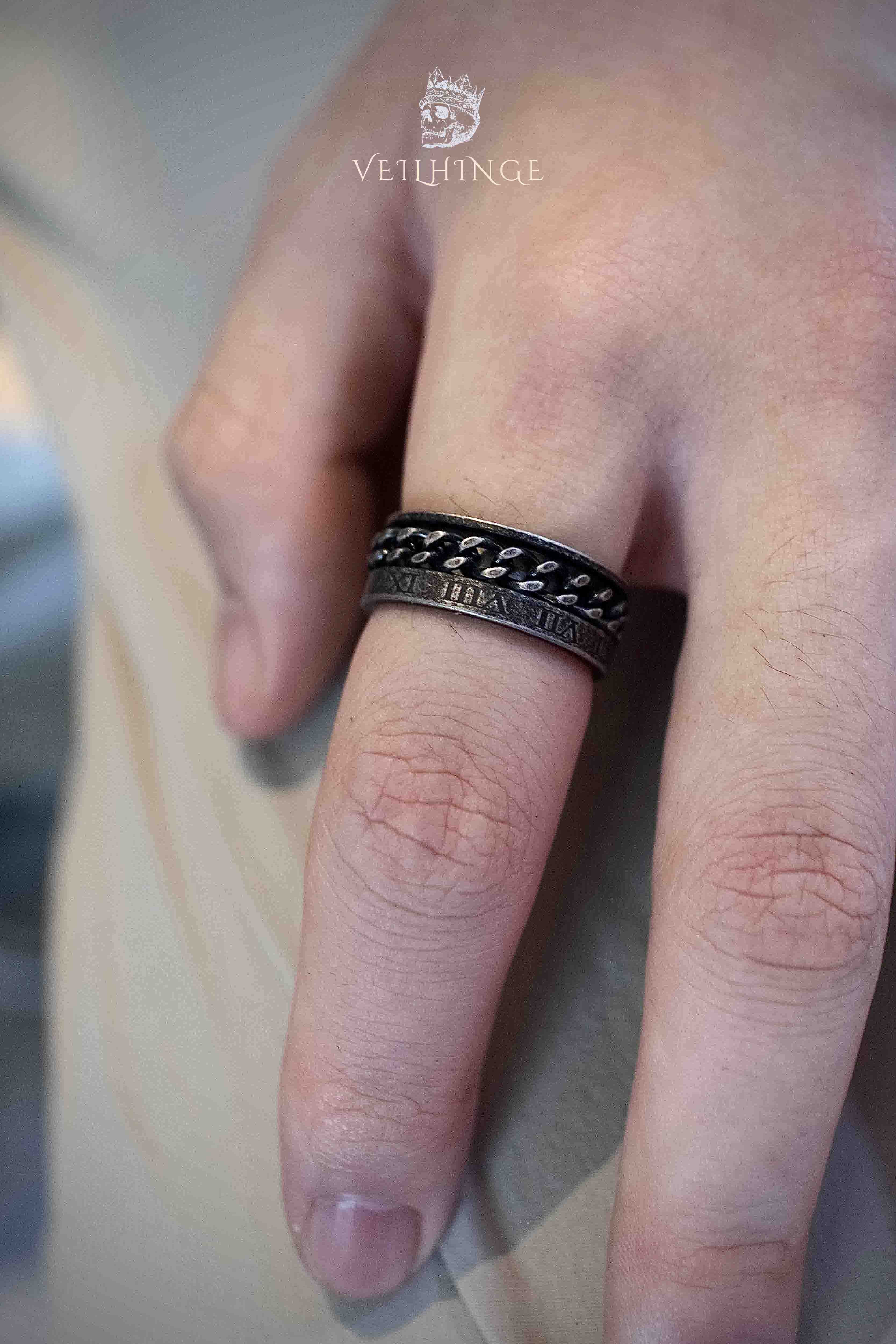 Chain spinner ring viewed from below showing Roman numeral inscription along the lower band edge, dark oxidized metal with bronze tones and rotating chain layer above