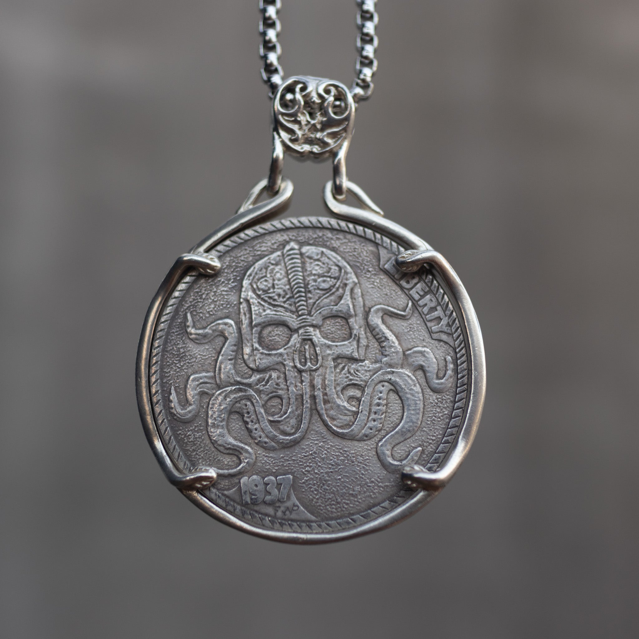 Close-up of a coin engraved with a skull whose lower face dissolves into spreading octopus tentacles, Liberty inscription, dated 1937, on dark stone surface