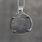 Cinco Pesos coin pendant featuring a skull-faced Cuauhtémoc in Aztec headdress, set in a four-prong bezel with skull bail on a box chain