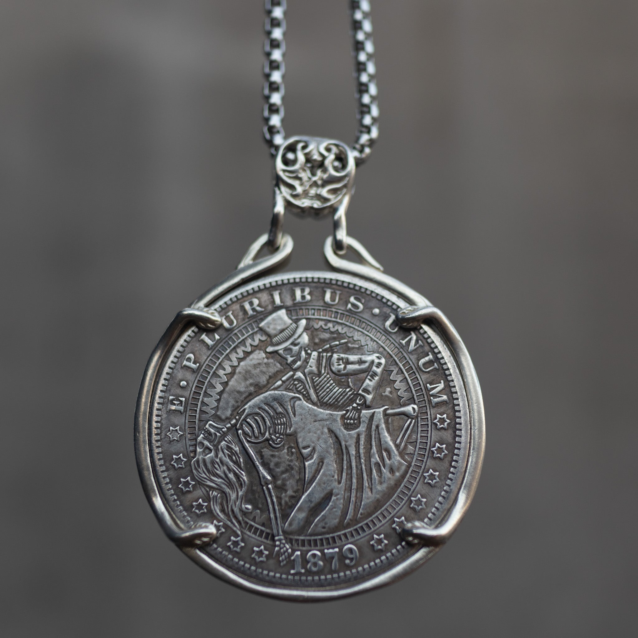 Coin pendant engraved with a skeleton couple dancing — a top-hatted gentleman skeleton leading a long-skirted female skeleton in a backbend, dated 1879, set in a four-prong bezel on a chain Main image