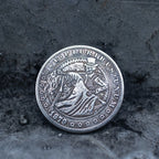 Close-up of a coin engraved with two skeletons dancing — male skeleton in top hat and suit leading a female skeleton in a long dress bending backward, E Pluribus Unum border, dated 1879