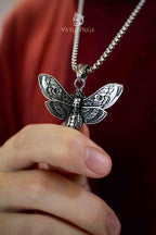 Death's head moth skull pendant necklace held in hand close-up, detailed engraved wings and skull motif, oxidized silver, gothic dark aesthetic necklace

