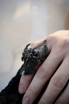 Full finger demon armor ring on a straightened hand with the eye closed, dark oxidized claw structure running along the finger from a side angle