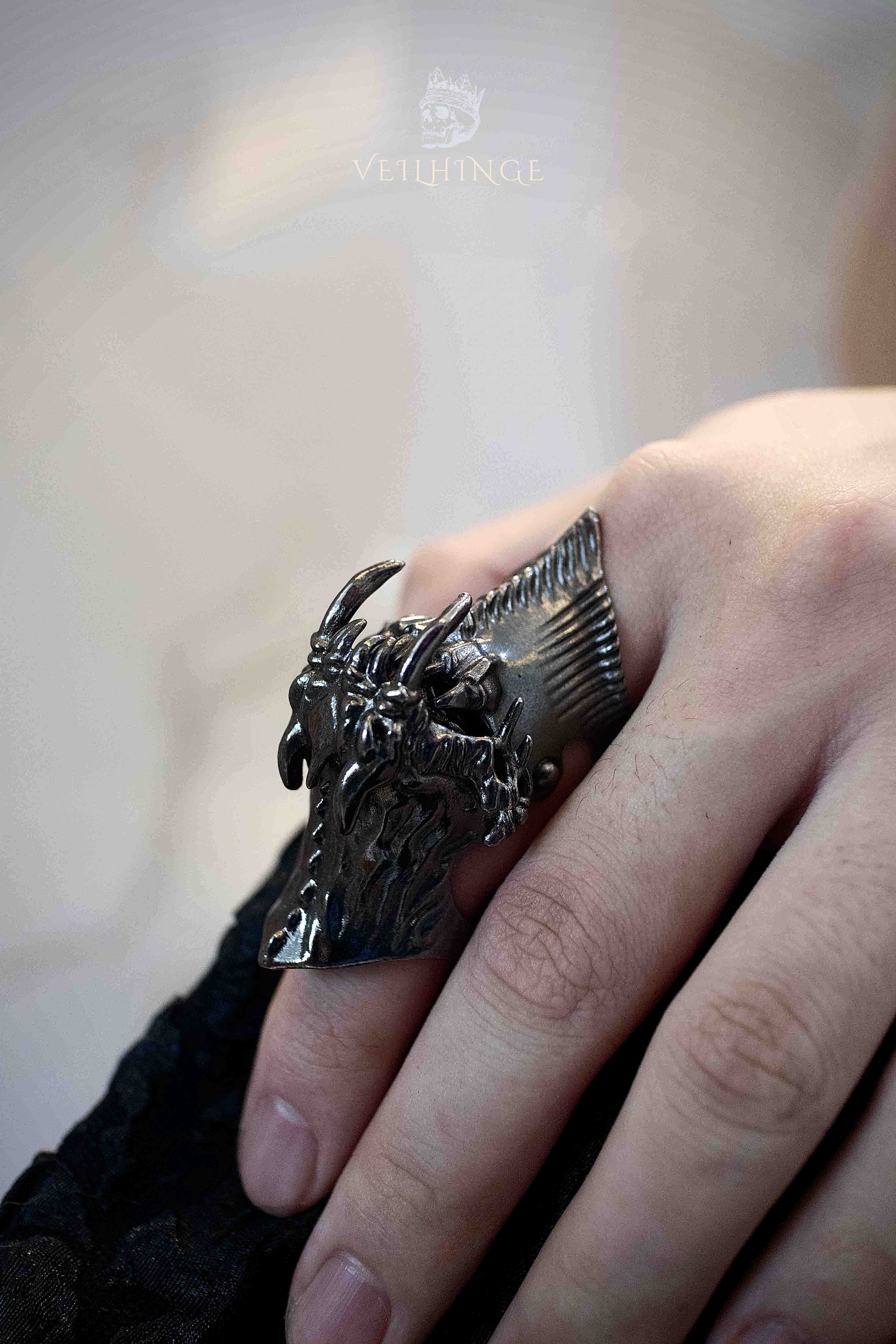 Full finger demon armor ring on a straightened hand with the eye closed, dark oxidized claw structure running along the finger from a side angle