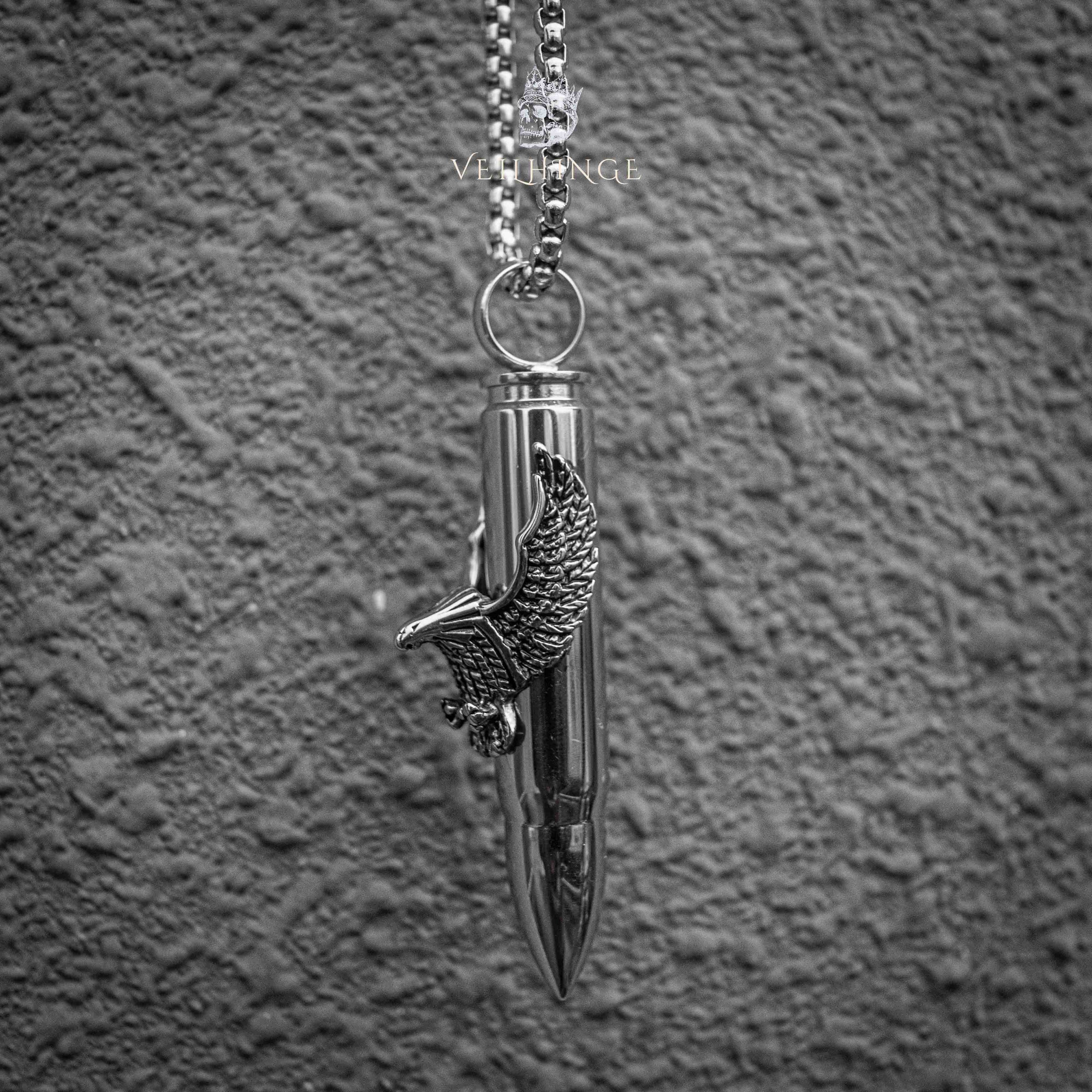 eagle wing bullet pendant close-up — spread wing motif gripping polished bullet casing, biker dark aesthetic necklace