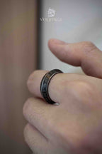Elder Futhark runic band ring resting on a rough stone surface, two rows of Norse runes carved into a dark oxidized wide band, photographed in natural grey light