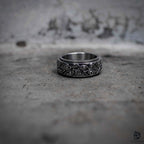 Evil eye spinning ring flat lay showing oxidized outer rotating band with eye engraving and polished inner band, dark aesthetic stainless steel fidget ring by Veilhinge