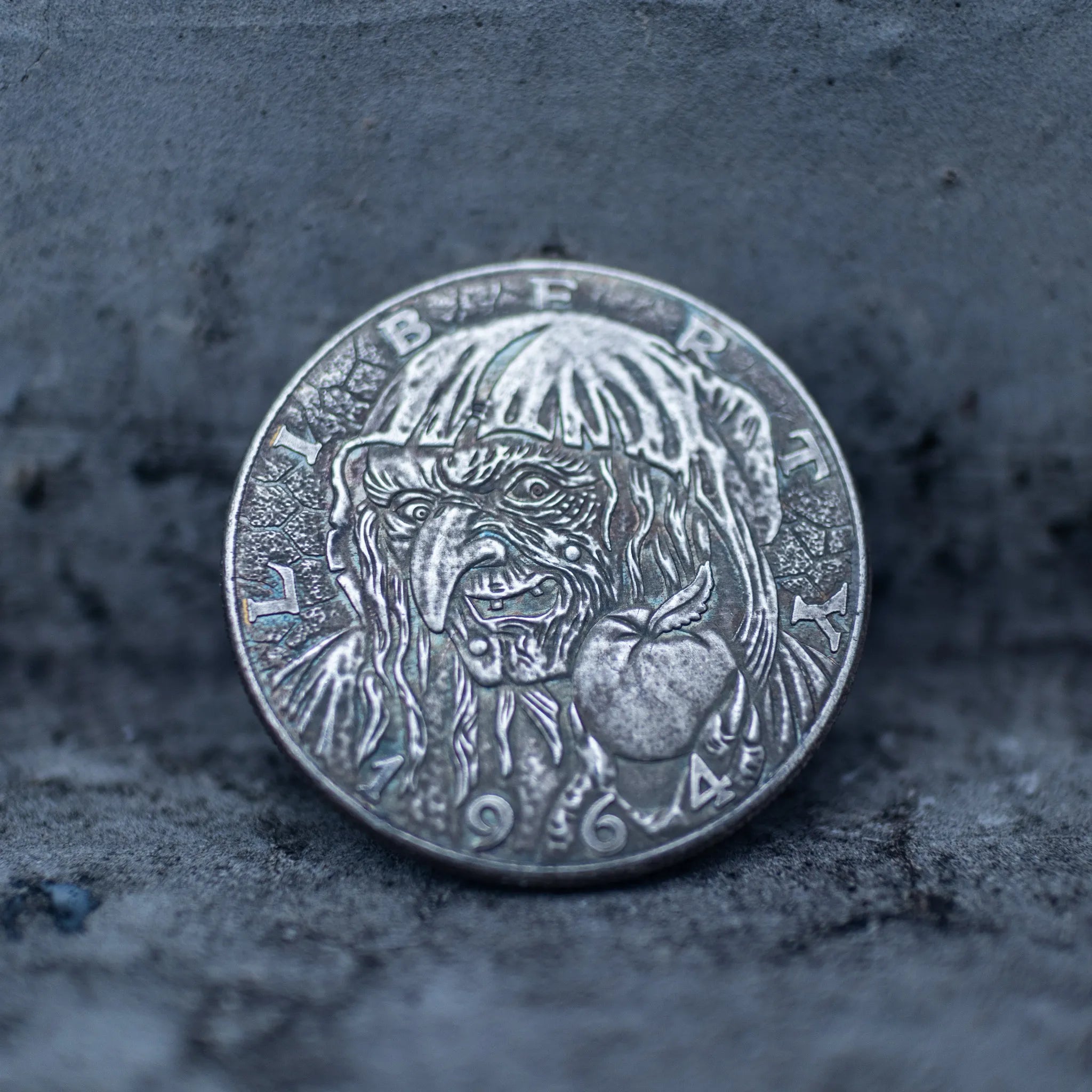Close-up of a coin engraved with the Evil Queen witch in hooded cloak, poison apple visible at lower right, dated 1964