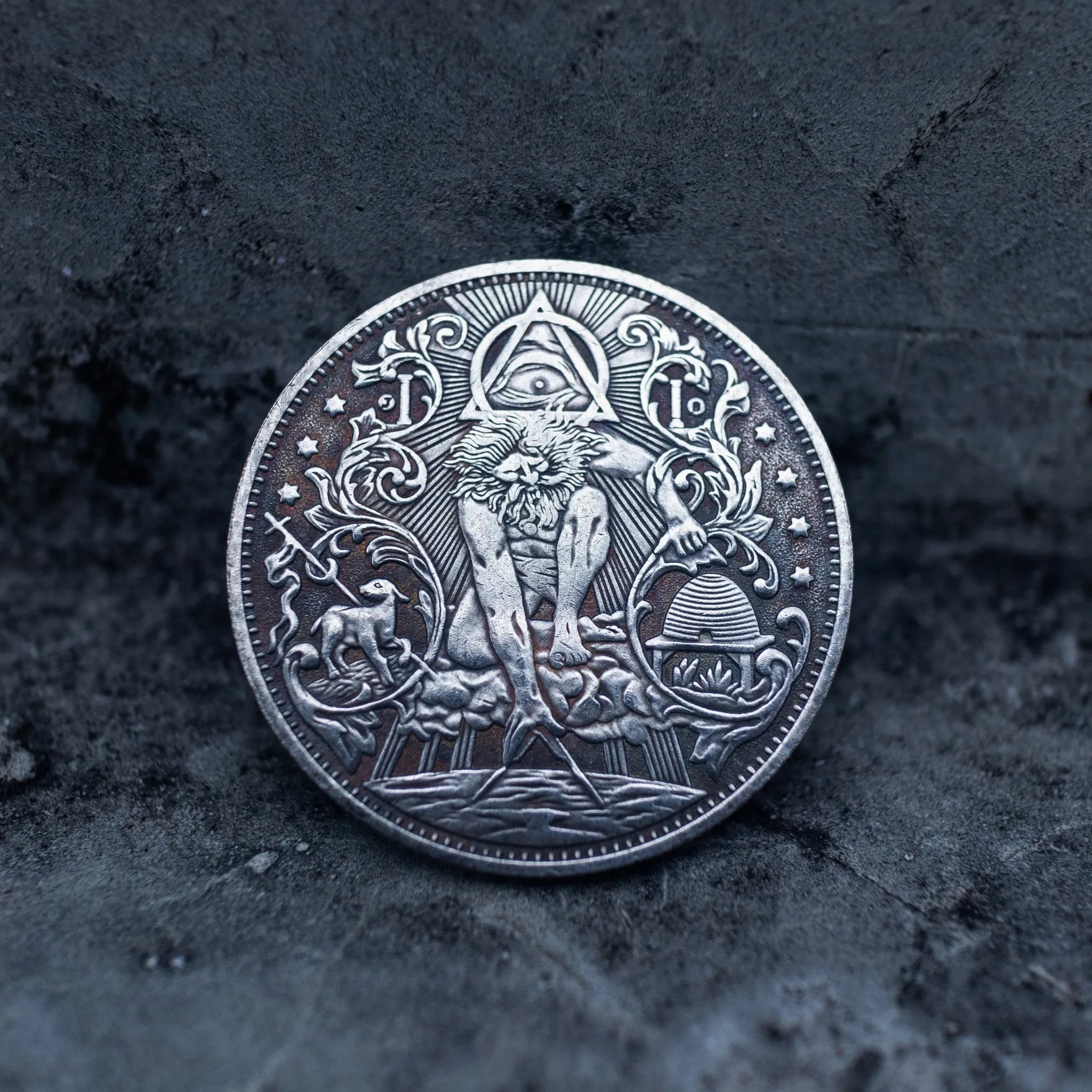 Close-up of a coin engraved with the Eye of Providence triangle, standing human figure, flanking deer and wolf, beehive at base, scrollwork border
