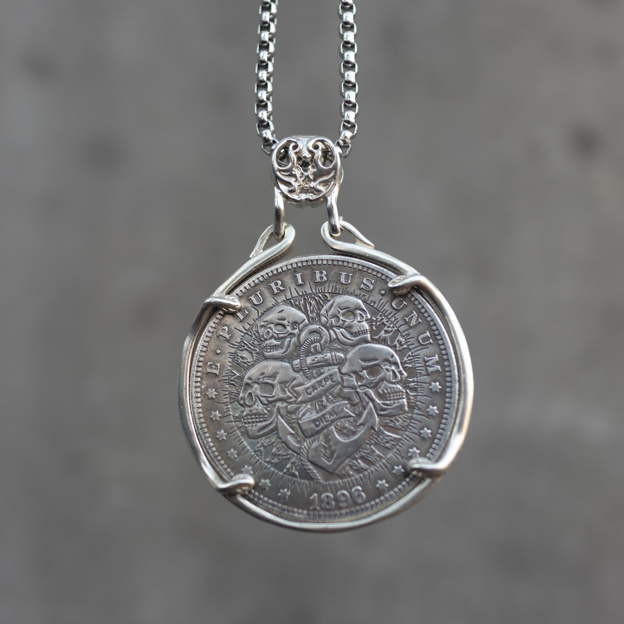Coin pendant engraved with four skulls arranged around an anchor bearing a Carpe Diem banner, radiant rays, E Pluribus Unum border, dated 1896, set in a four-prong bezel on a chain