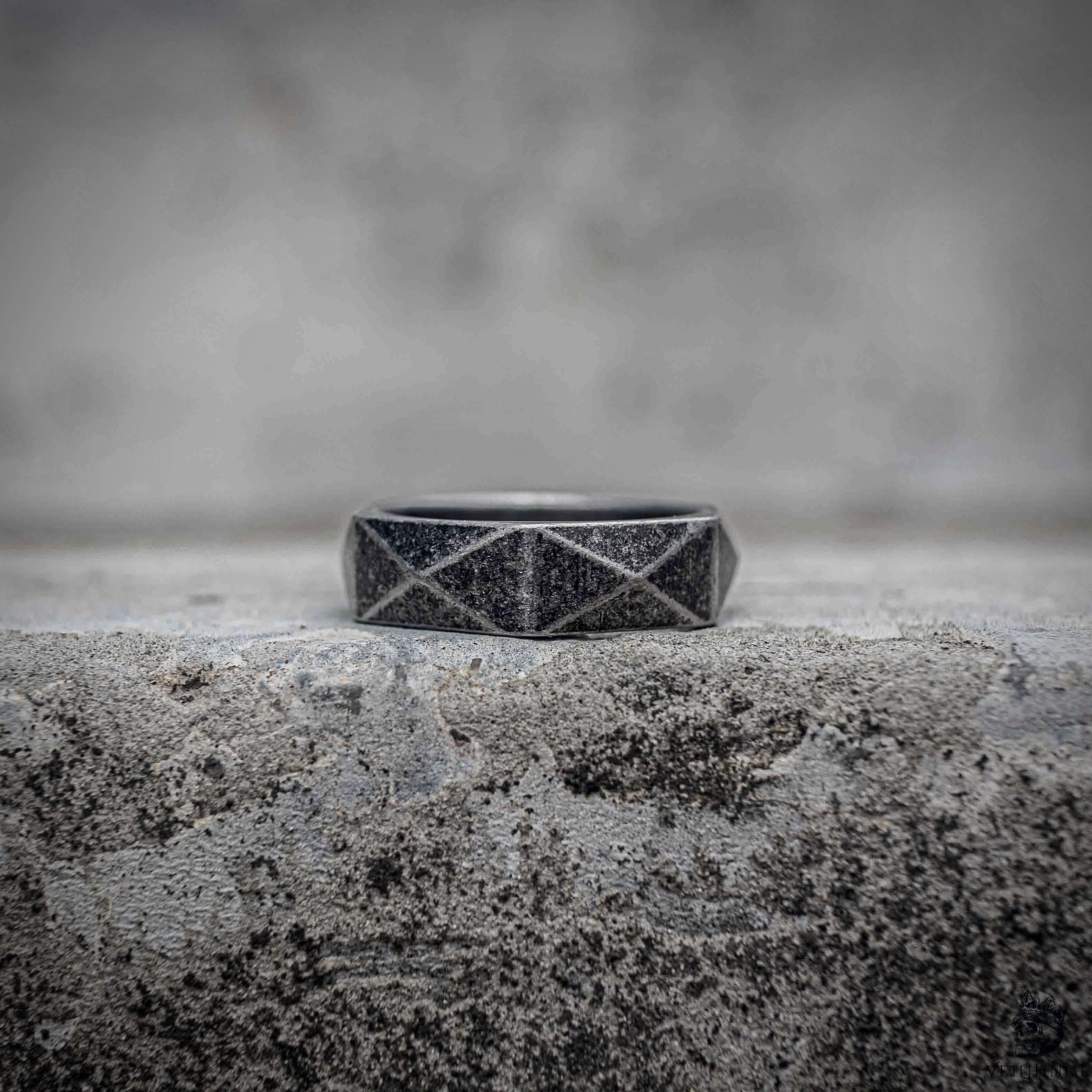 Geometric diamond faceted band ring with sandblasted oxidized black surface and polished cut lines in stainless steel, minimalist dark aesthetic ring by Veilhinge, front view