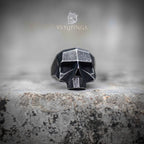 Side profile of geometric skull ring showing oxidized exterior and brushed steel inner band — angular low-poly construction on stone surface