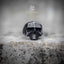 Side profile of geometric skull ring showing oxidized exterior and brushed steel inner band — angular low-poly construction on stone surface