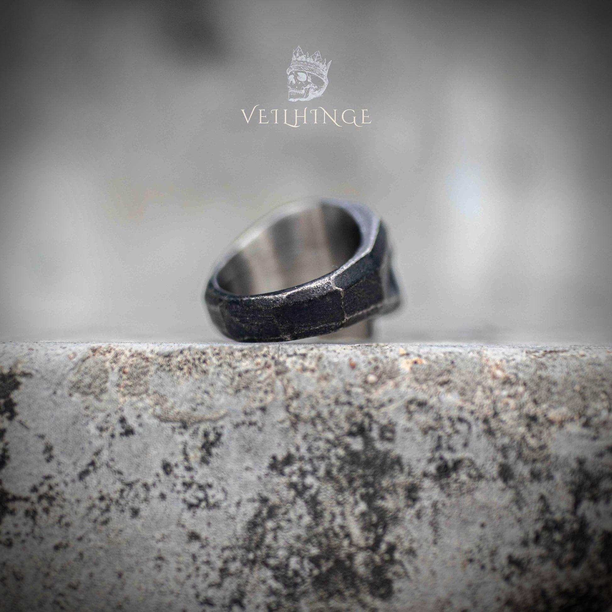 Front-facing geometric skull ring — faceted low-poly skull with oxidized dark finish, sharp angular planes catching light on stone